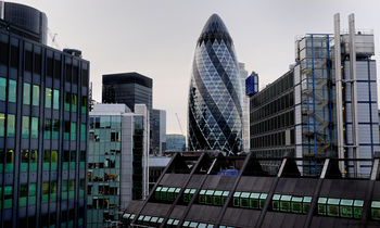 London offices and Gherkin This urban architecture photograph captures a view of city offices in London, United Kingdom, during the late afternoon in the early autumn season. The main subject of the image is the prominent Gherkin building, also known as 30 St Mary Axe, which stands out among the modern glass and steel structures that define the city skyline. The photograph highlights the dense concentration of high-rise office buildings, reflecting the characteristic architectural style of London's financial district, with the iconic Gherkin serving as a recognizable landmark in the heart of the city.